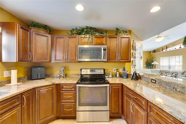 kitchen featuring light tile patterned floors, ceiling fan, appliances with stainless steel finishes, lofted ceiling, and light stone countertops