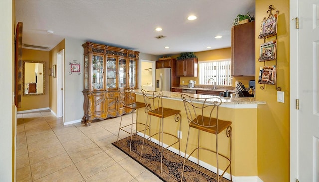 kitchen featuring light tile patterned floors, a kitchen bar, kitchen peninsula, stainless steel fridge, and sink