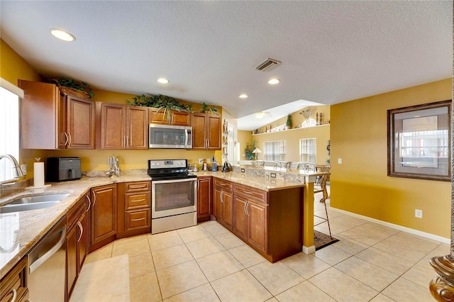 kitchen with light tile patterned floors, kitchen peninsula, sink, and stainless steel appliances