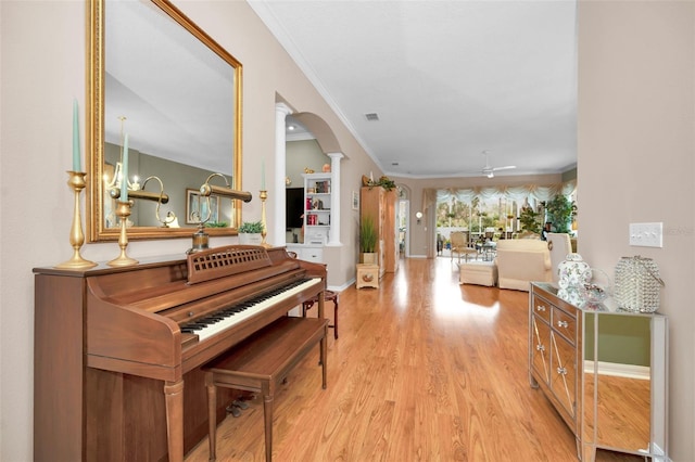 miscellaneous room with crown molding, light hardwood / wood-style flooring, ceiling fan with notable chandelier, and ornate columns