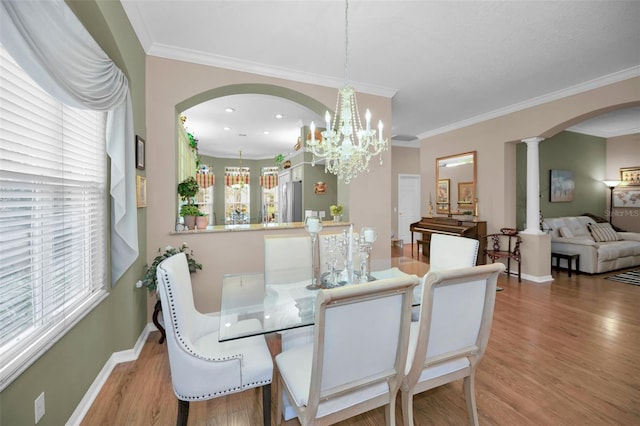 dining area featuring light hardwood / wood-style floors, crown molding, a chandelier, and ornate columns