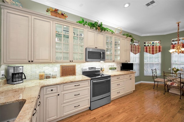 kitchen with appliances with stainless steel finishes, ornamental molding, hanging light fixtures, and light stone countertops