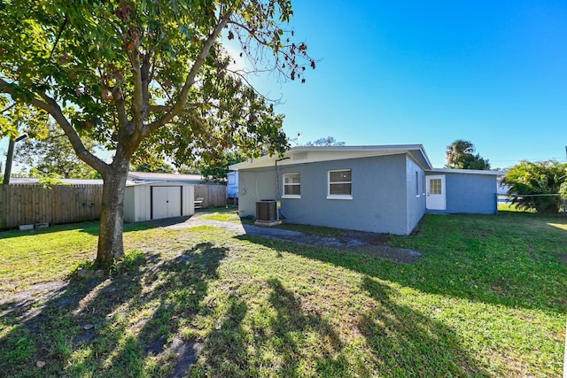 back of property featuring a shed, cooling unit, and a yard