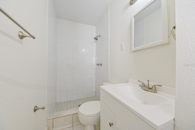 bathroom featuring toilet, a tile shower, tile patterned floors, and vanity