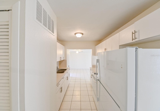 kitchen with white cabinets, sink, light tile patterned floors, and white refrigerator