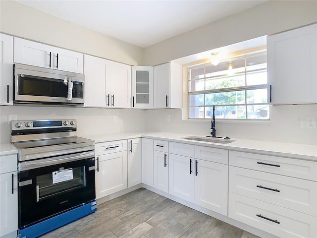 kitchen with white cabinets, light hardwood / wood-style flooring, appliances with stainless steel finishes, and sink