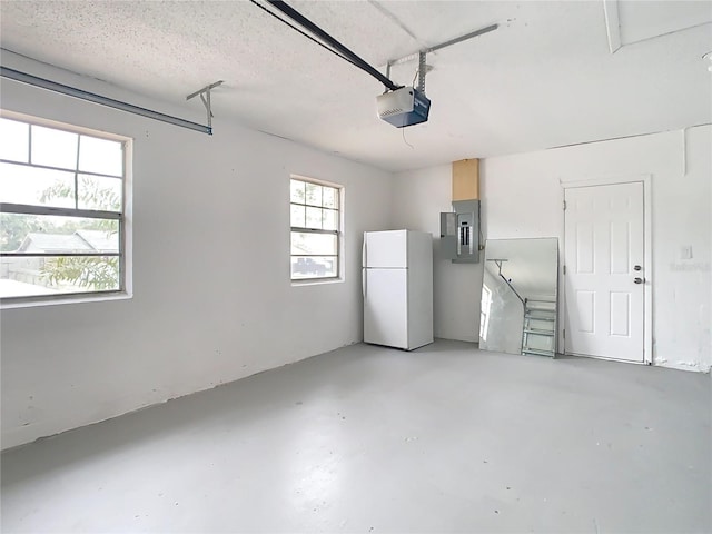 garage featuring electric panel, white fridge, and a garage door opener