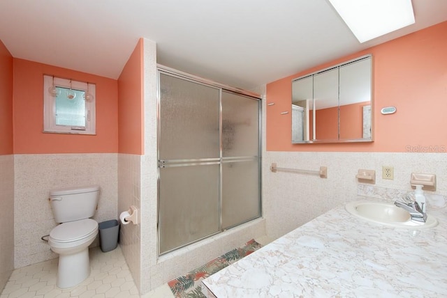 bathroom with tile patterned floors, vanity, tile walls, toilet, and a shower with shower door