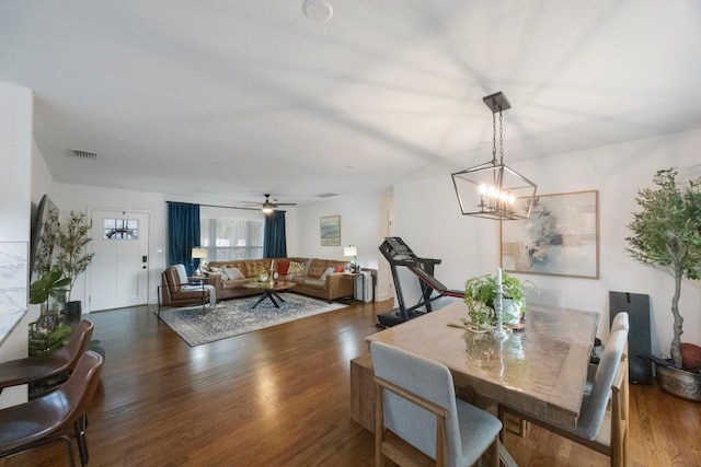 dining space with ceiling fan with notable chandelier and dark hardwood / wood-style flooring