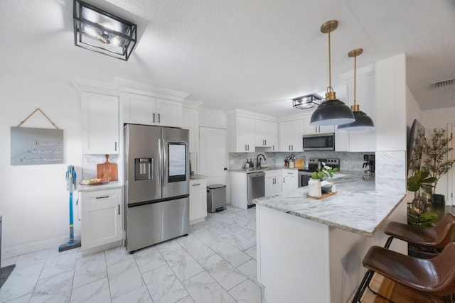 kitchen featuring pendant lighting, kitchen peninsula, decorative backsplash, appliances with stainless steel finishes, and white cabinets