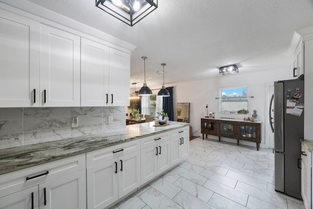 kitchen featuring backsplash, stainless steel fridge, white cabinetry, and pendant lighting