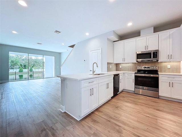 kitchen with kitchen peninsula, sink, white cabinetry, light wood-type flooring, and stainless steel appliances