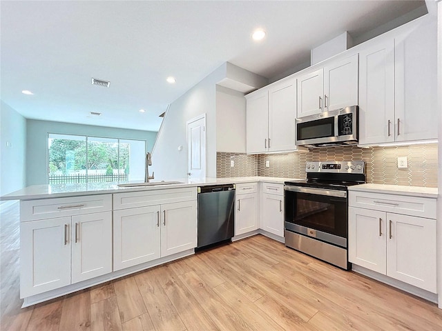 kitchen with kitchen peninsula, sink, stainless steel appliances, and white cabinetry