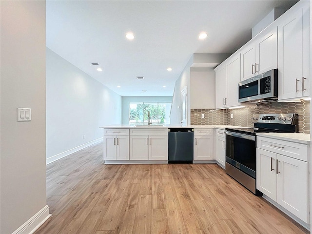 kitchen with kitchen peninsula, appliances with stainless steel finishes, white cabinets, light hardwood / wood-style flooring, and sink