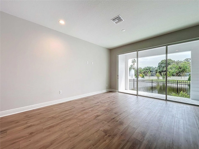 unfurnished room with a water view, wood-type flooring, and a textured ceiling