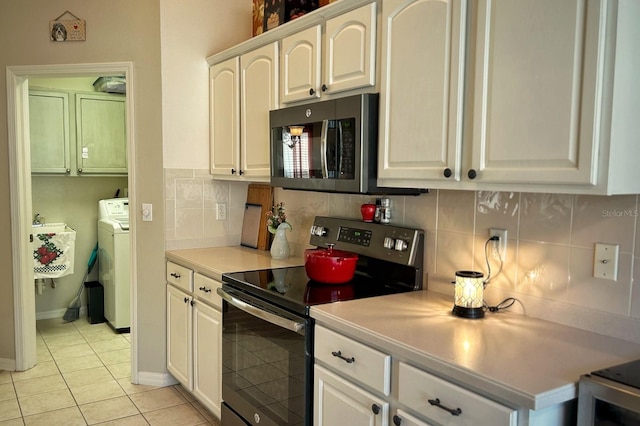 kitchen featuring appliances with stainless steel finishes, tasteful backsplash, white cabinets, light tile patterned floors, and washer and clothes dryer