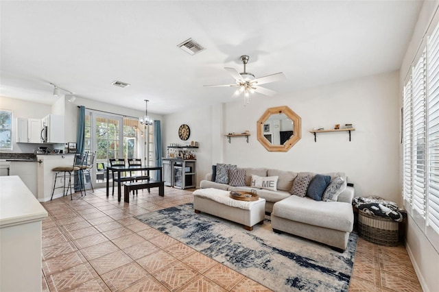 tiled living room featuring ceiling fan with notable chandelier