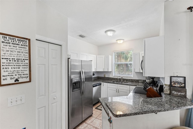 kitchen with dark stone countertops, kitchen peninsula, sink, white cabinetry, and appliances with stainless steel finishes