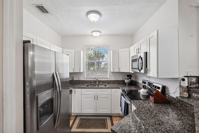 kitchen with sink, stainless steel appliances, a textured ceiling, white cabinets, and dark stone counters