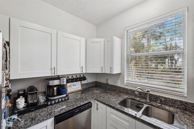 kitchen featuring stainless steel dishwasher, sink, white cabinetry, a textured ceiling, and dark stone counters