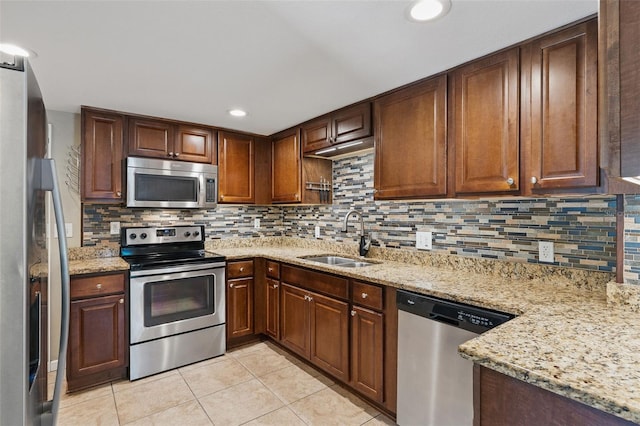 kitchen featuring a sink, backsplash, light stone countertops, and appliances with stainless steel finishes