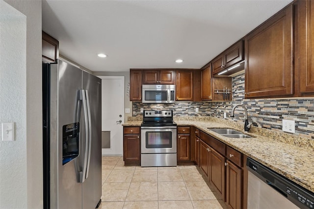 kitchen with stainless steel appliances, decorative backsplash, a sink, light tile patterned flooring, and light stone counters