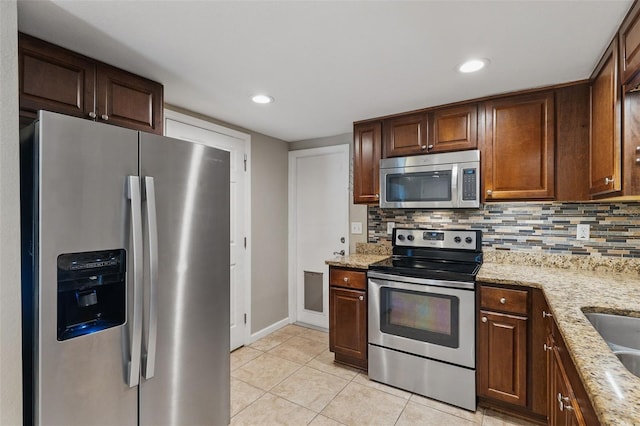 kitchen with light tile patterned flooring, backsplash, light stone countertops, and appliances with stainless steel finishes