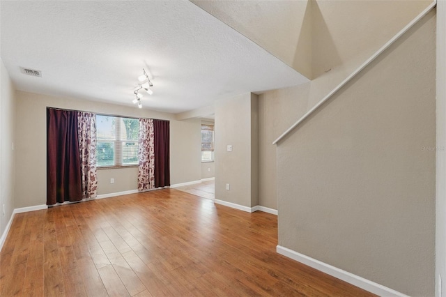 unfurnished room featuring stairway, light wood-type flooring, baseboards, a textured ceiling, and visible vents