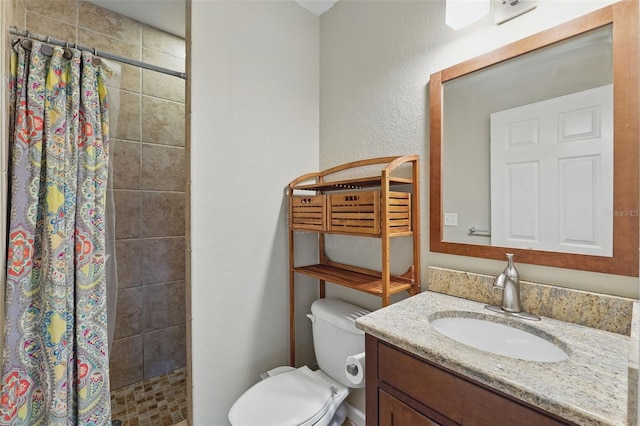 bathroom with a textured wall, a tile shower, toilet, and vanity