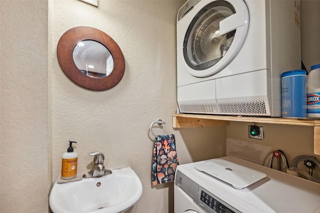 bathroom featuring a textured wall, stacked washer and clothes dryer, and a sink