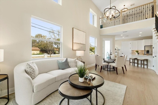 living room with light wood-type flooring, a towering ceiling, a wealth of natural light, and a chandelier