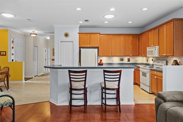 kitchen with white appliances, a center island, light wood-type flooring, crown molding, and a breakfast bar area