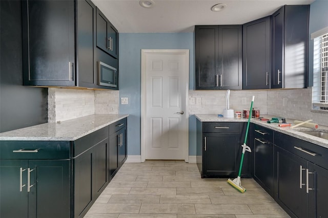 kitchen featuring stainless steel microwave, backsplash, and light stone countertops