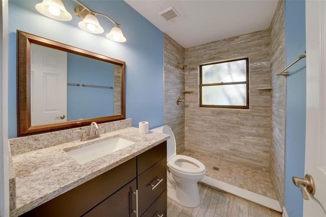 bathroom featuring toilet, tiled shower, and vanity