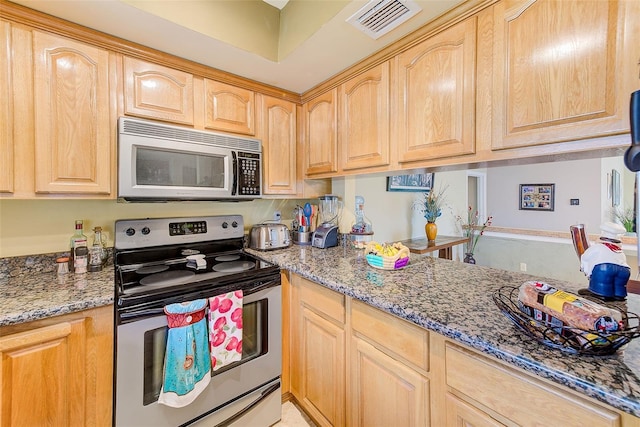 kitchen featuring dark stone countertops, light brown cabinetry, and stainless steel appliances