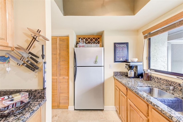 kitchen with light tile patterned flooring, refrigerator, sink, dark stone countertops, and light brown cabinets