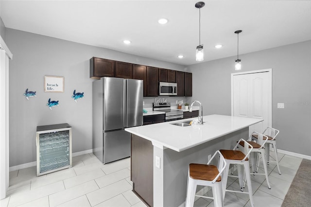 kitchen with an island with sink, appliances with stainless steel finishes, decorative light fixtures, dark brown cabinets, and sink