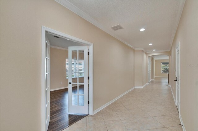 corridor featuring crown molding, light tile patterned floors, a textured ceiling, and ornate columns