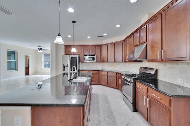 kitchen with light tile patterned flooring, sink, hanging light fixtures, stainless steel appliances, and a center island with sink