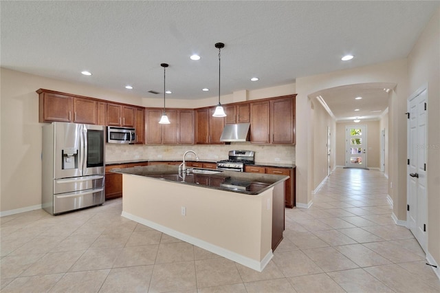 kitchen featuring appliances with stainless steel finishes, pendant lighting, sink, backsplash, and a center island with sink