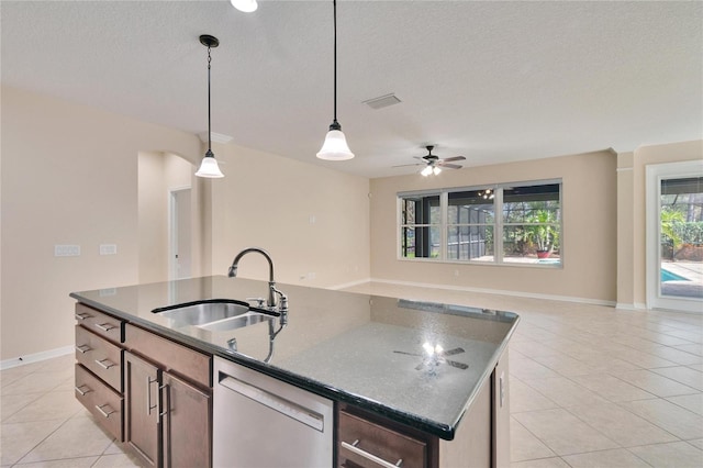 kitchen featuring sink, a kitchen island with sink, hanging light fixtures, dark stone countertops, and stainless steel dishwasher