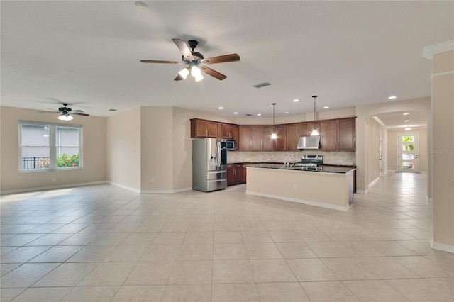 kitchen featuring tasteful backsplash, decorative light fixtures, light tile patterned floors, an island with sink, and stainless steel appliances