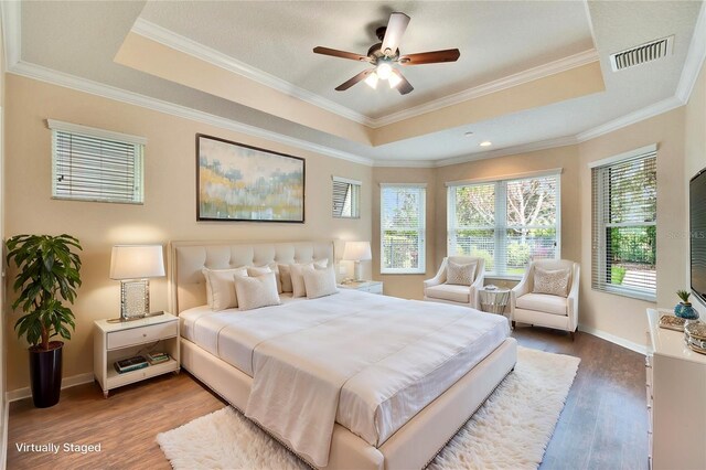 bedroom featuring a raised ceiling, hardwood / wood-style floors, and multiple windows