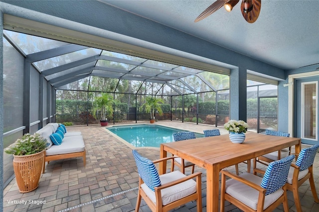 view of pool with ceiling fan, a patio, outdoor lounge area, and glass enclosure