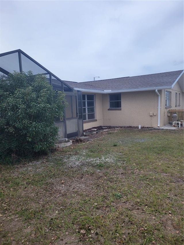 rear view of property featuring a lawn and glass enclosure