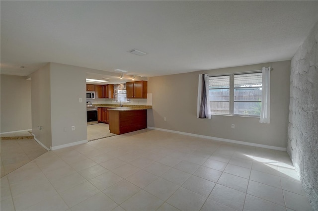 kitchen with appliances with stainless steel finishes, kitchen peninsula, sink, and light tile patterned floors