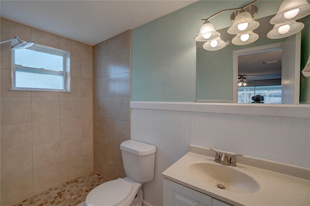 bathroom with wooden walls, vanity, tiled shower, toilet, and a textured ceiling