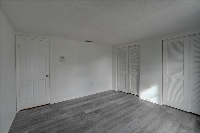 unfurnished bedroom featuring multiple closets, a textured ceiling, and light hardwood / wood-style floors