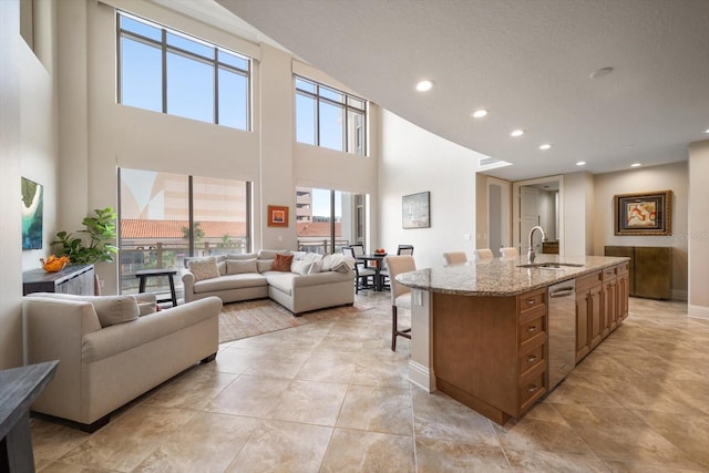 kitchen featuring a center island with sink, a breakfast bar area, stainless steel dishwasher, light stone counters, and sink