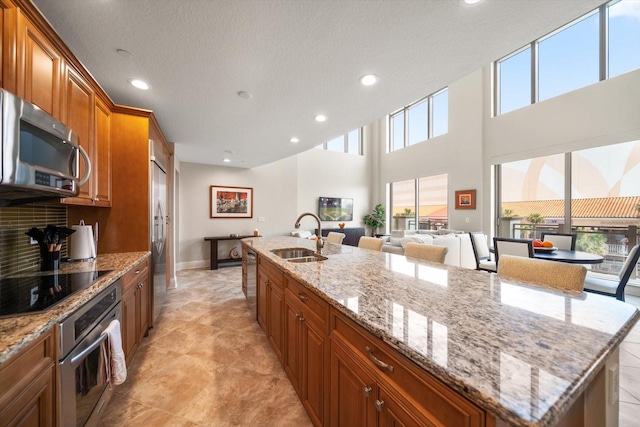 kitchen with stainless steel appliances, a center island with sink, light stone counters, and sink